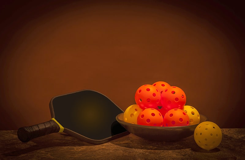 Pickleball still life with bowl of Pickleballs and Paddle on a b AdobeStock 194795516