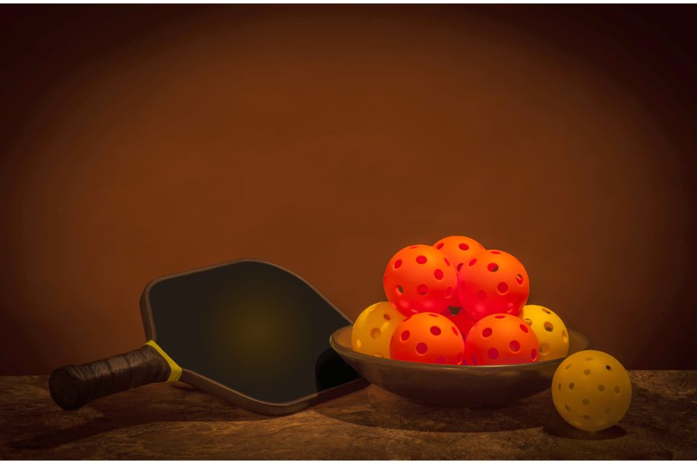 What Kind of Ball is Used in Pickleball? 2 Pickleballs and Paddle on a brown background